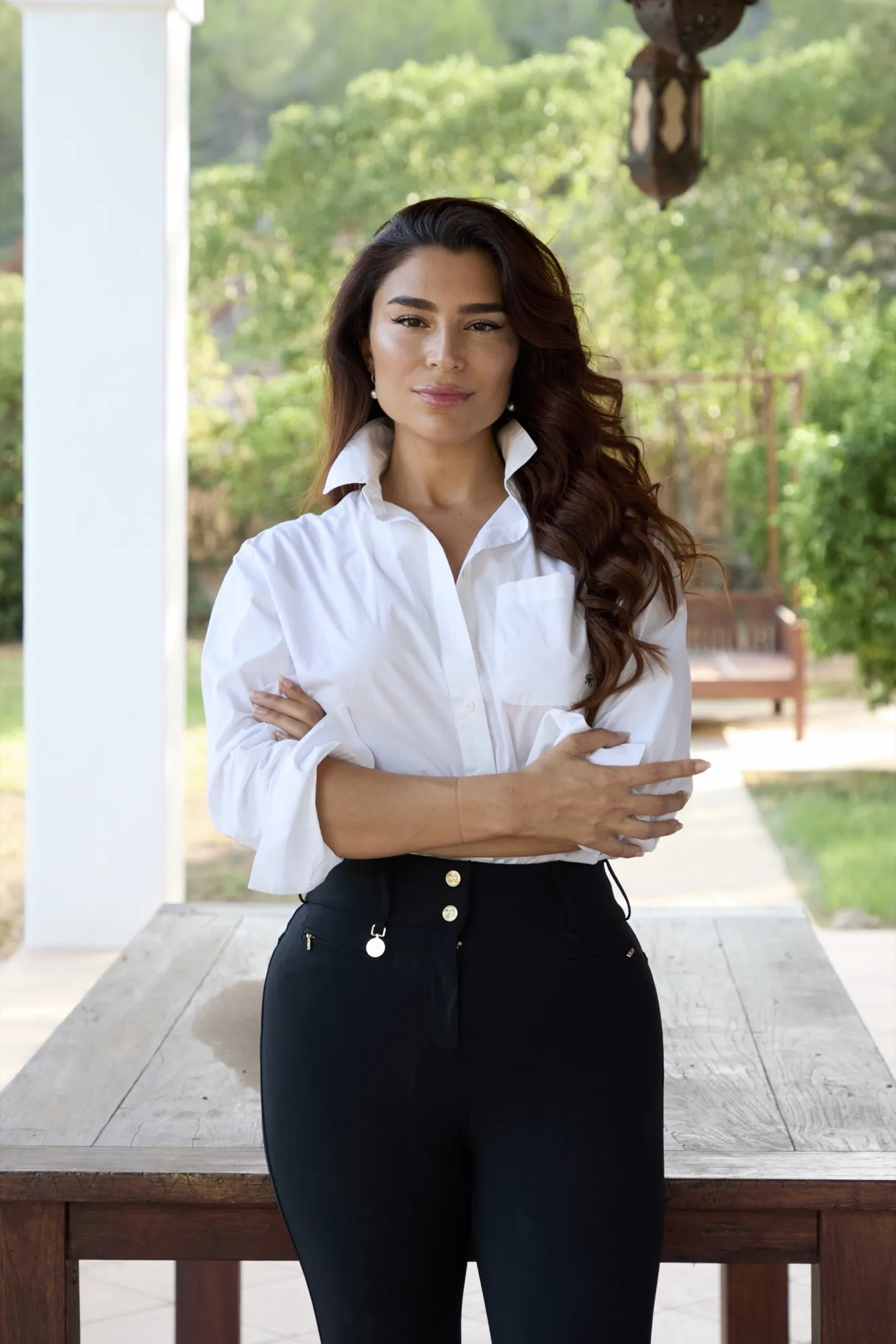 Handan Darici in a white shirt, arms folded, on a garden terrace